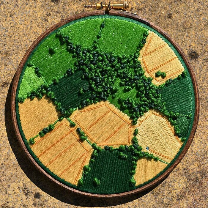 a close up of a embroidery on a wooden hoop with green and yellow fields in the background