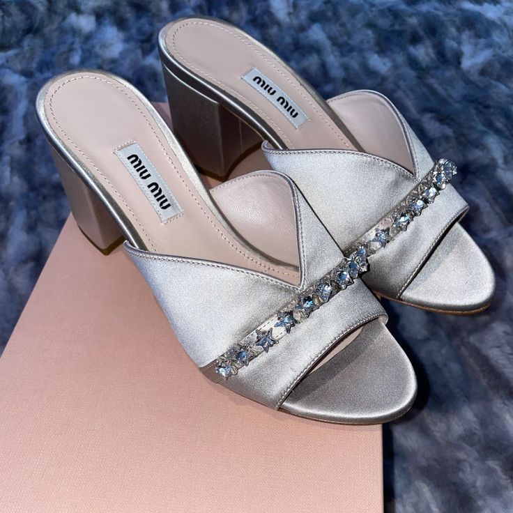 Silver Satin Fabric Mules With Silver Star Detail. Nwb Heel Size Approx 3.5 Inches Luxury Open Toe Sandals By Miu Miu, Miu Miu Elegant Block Heel Heels, Elegant Miu Miu Block Heel Heels, Luxury Miu Miu Heels For Summer, Luxury Miu Miu Summer Heels, Elegant Miu Miu Block Heels, Luxury Open Toe Miu Miu Heels, Luxury Open Toe Heels By Miu Miu, Luxury Miu Miu Open Toe Heels