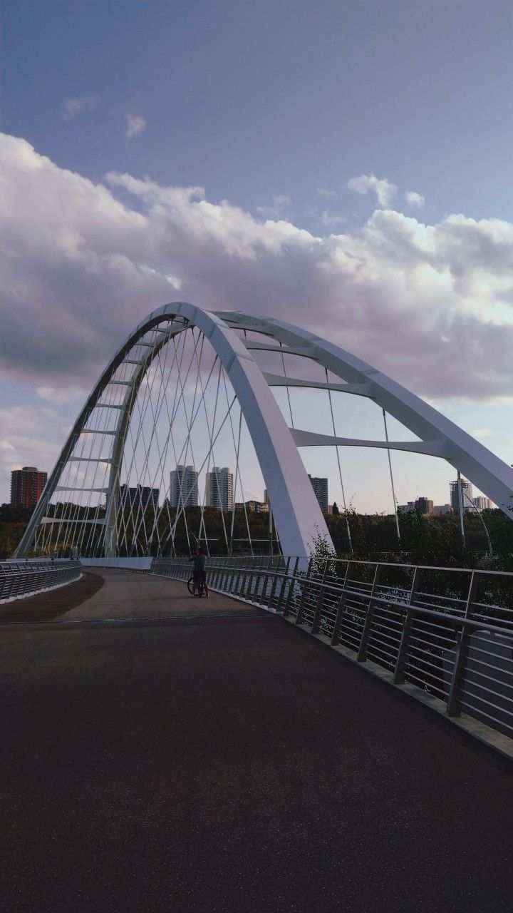 a man riding a skateboard across a bridge next to a tall white building with a sky background