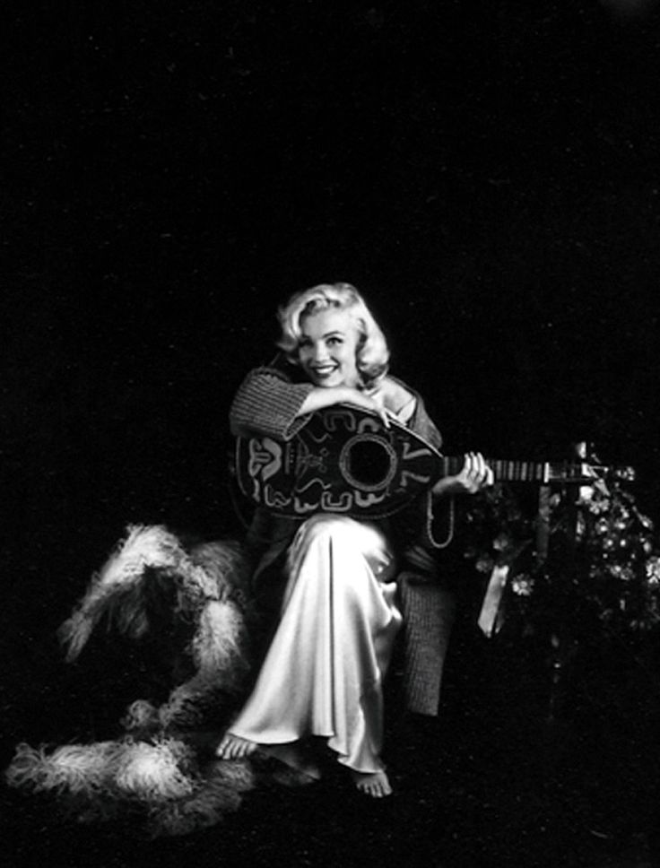 a black and white photo of a woman sitting on a chair with a guitar in her hand