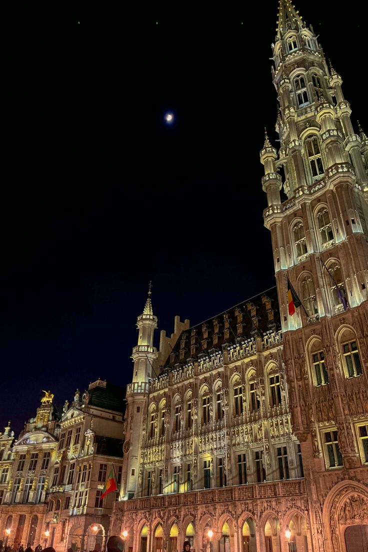 an old building lit up at night with the moon in the sky