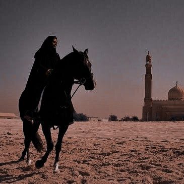 a man riding on the back of a black horse in front of a tall building