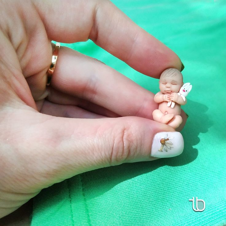 a person holding a tiny figurine in their left hand and wearing a ring