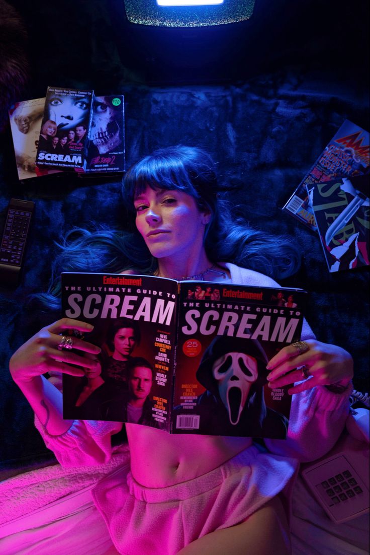 a woman laying in bed holding up a magazine with the word scream on it's cover