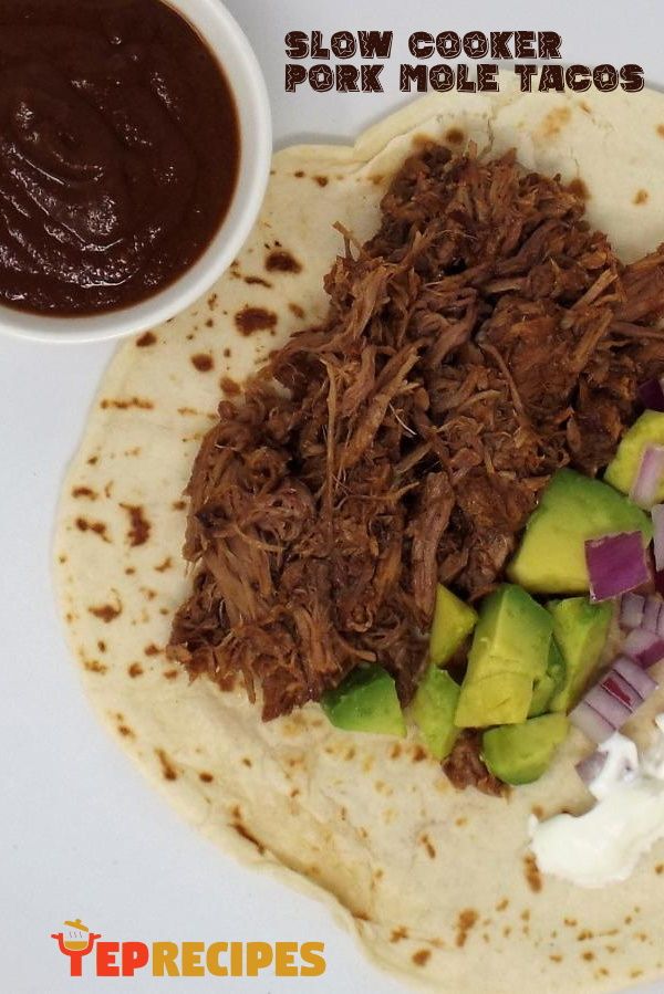 a tortilla with meat, onions and avocado on it next to a bowl of sauce