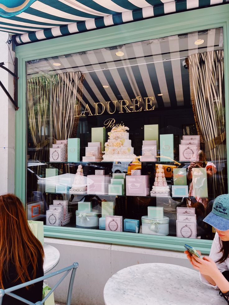 two women sitting at a table in front of a store window looking at their cell phones