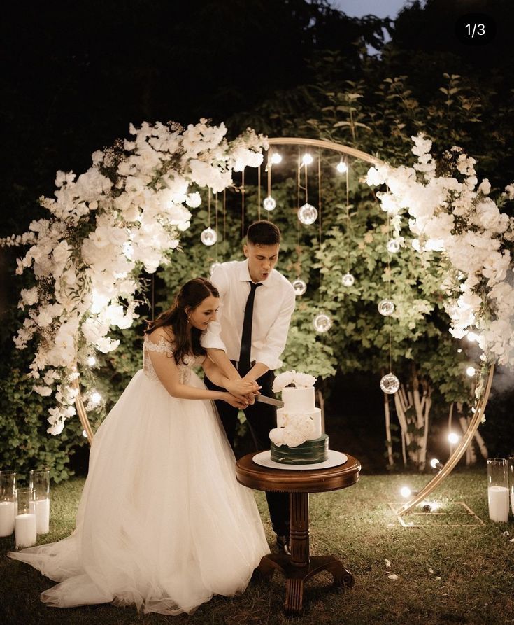 a bride and groom cutting their wedding cake in front of an arch with candles on it