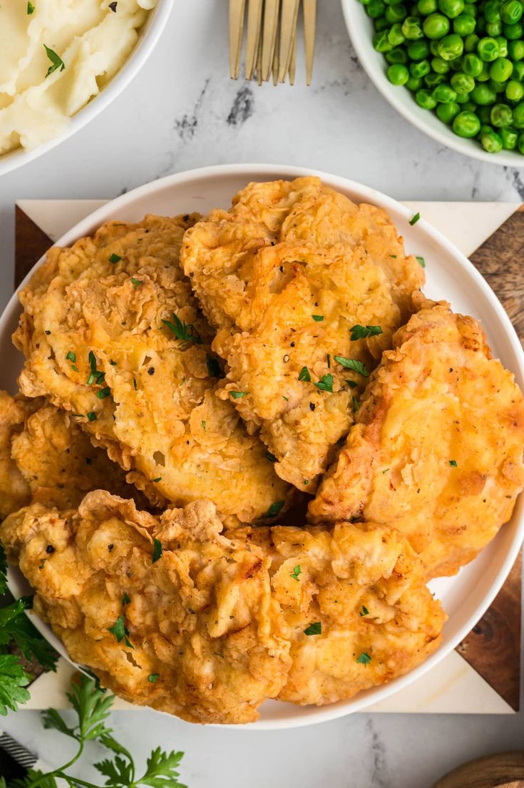 fried chicken and mashed potatoes on a white plate with peas, parmesan cheese and green peas