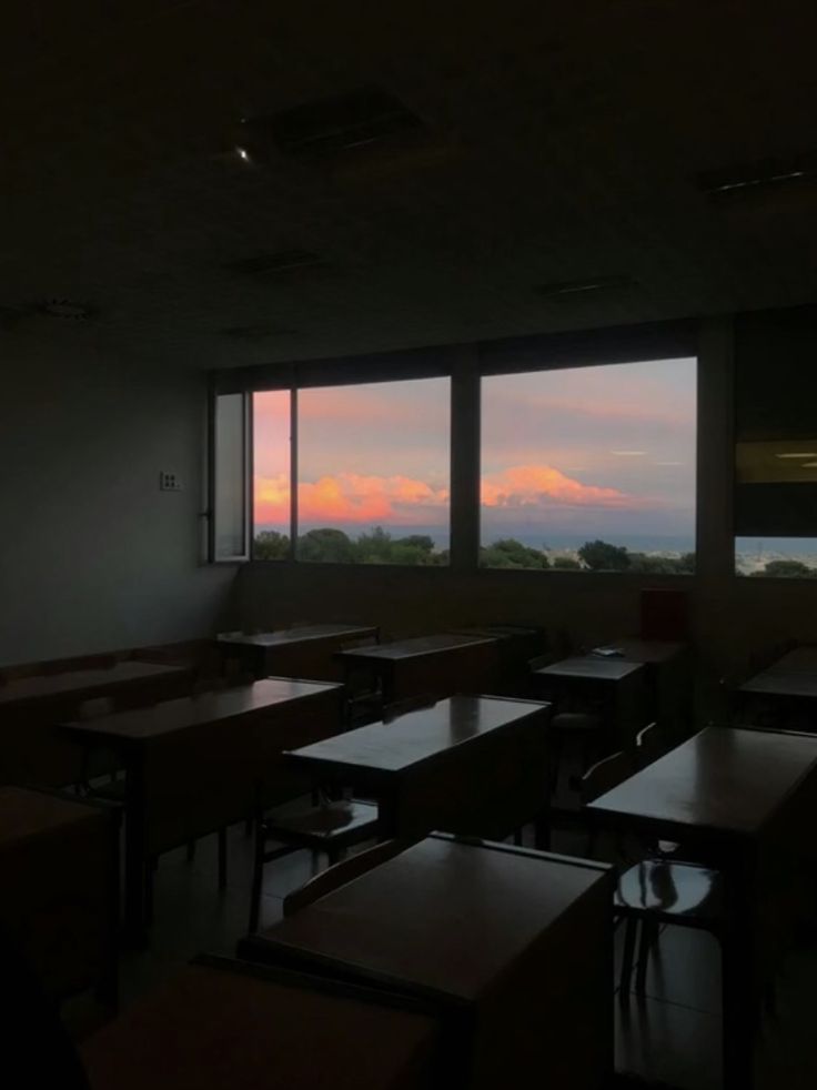 an empty classroom with desks and windows looking out on the mountains outside at sunset