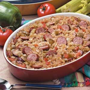 a casserole dish filled with sausage and vegetables next to asparagus on a table