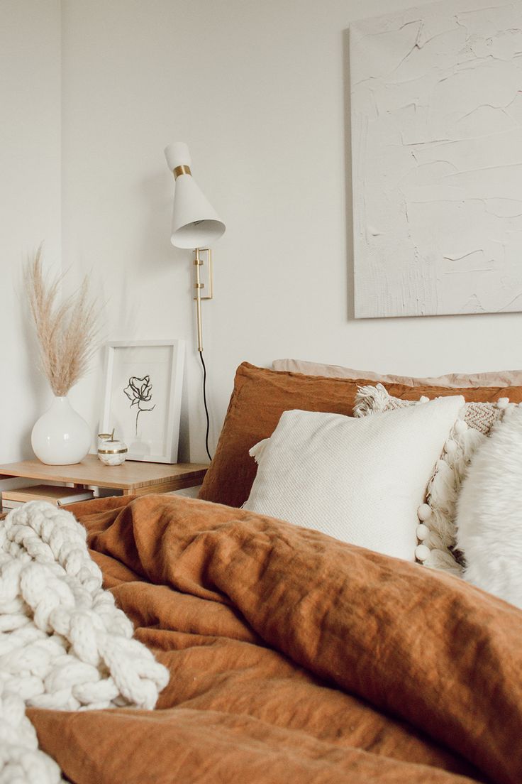 a bed with blankets and pillows on top of it next to a nightstand in a white room