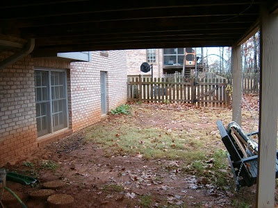 an empty back yard with a bench in the foreground and a brick house in the background