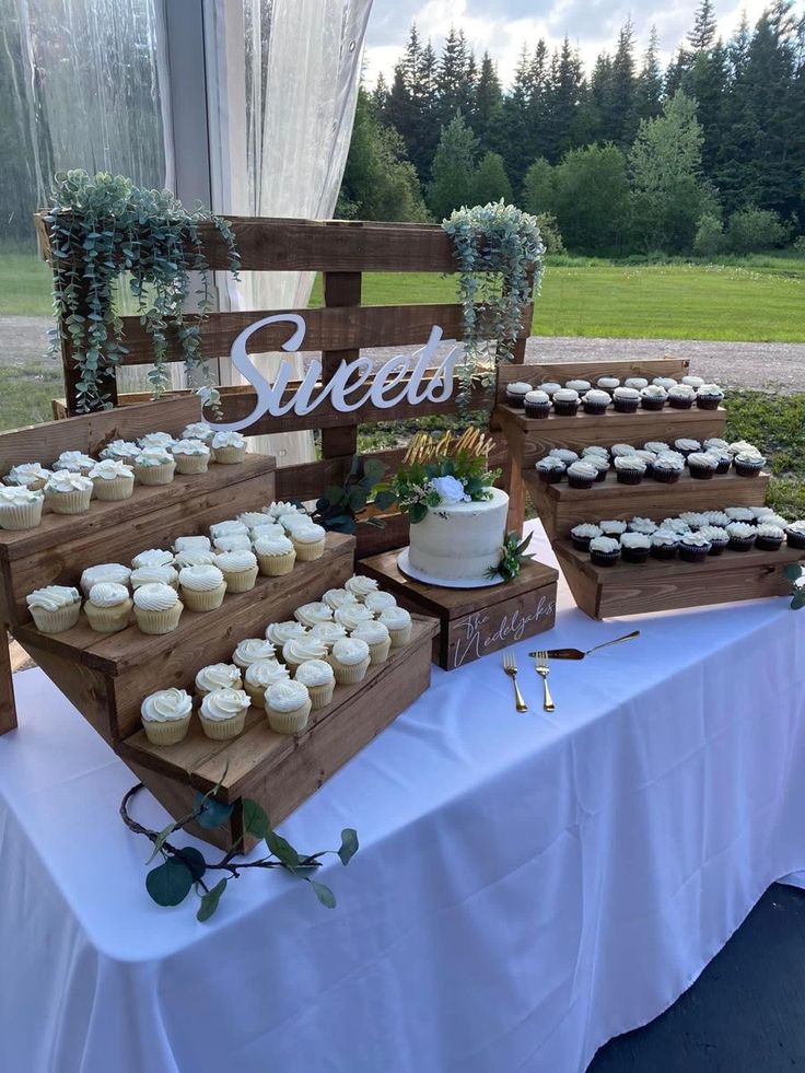 a table topped with lots of cupcakes next to a wooden sign that says sweet