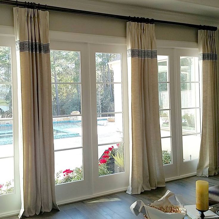 a living room filled with furniture and windows covered in drapes next to a pool