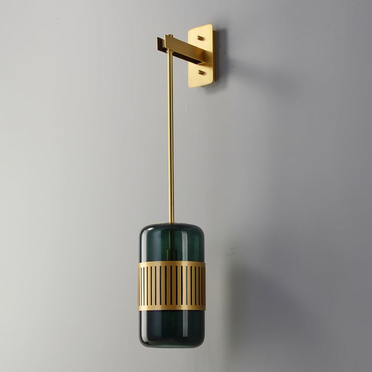 a green and gold light hanging from a wall next to a gray wall with a white background