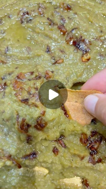 a hand holding a wooden spoon over a bowl filled with green sauce and other food