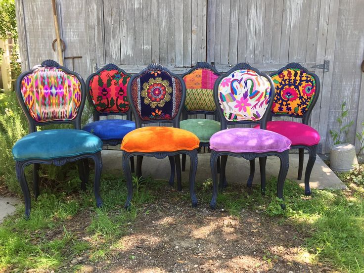 six colorful chairs lined up in front of a wooden fence with an artistic design on them