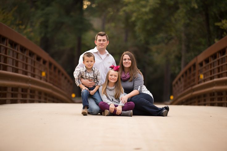 a family poses on a bridge in the woods for a portrait session with their two children