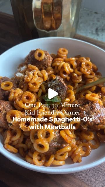 a white bowl filled with pasta and meatballs on top of a wooden table next to a glass bottle