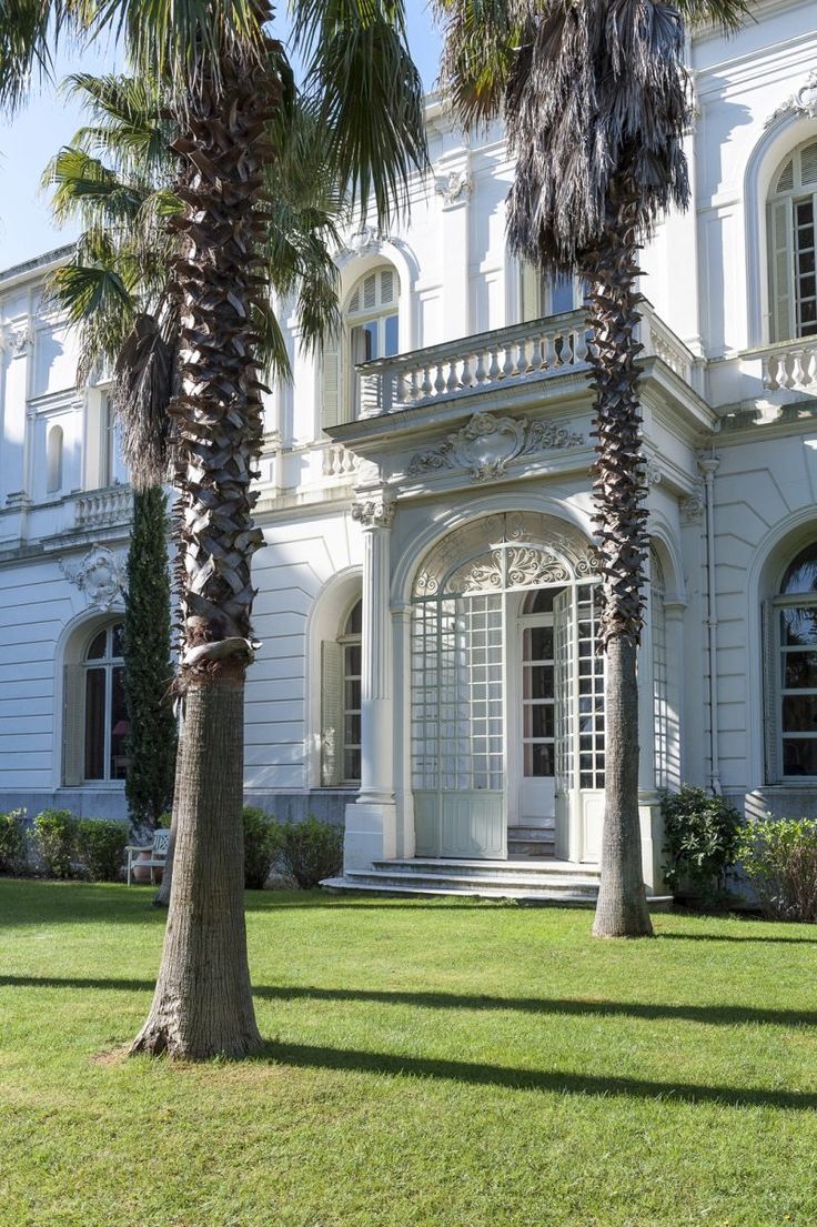 two palm trees are in front of a large white building with arched windows and balconies