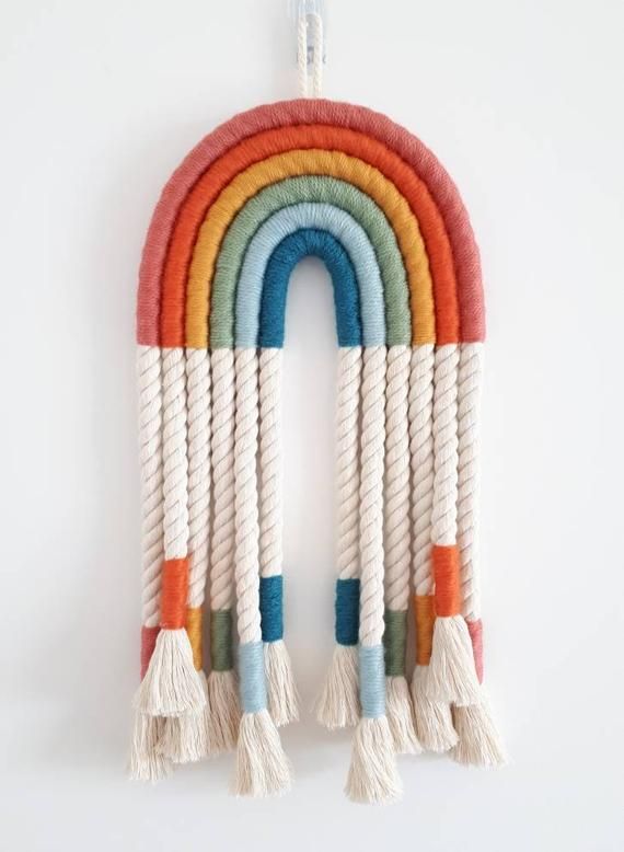 a multicolored rainbow hanging on a white wall with tassels and ropes