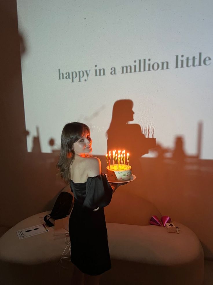 a woman holding a cake with lit candles in front of a projection screen that says happy in a million little