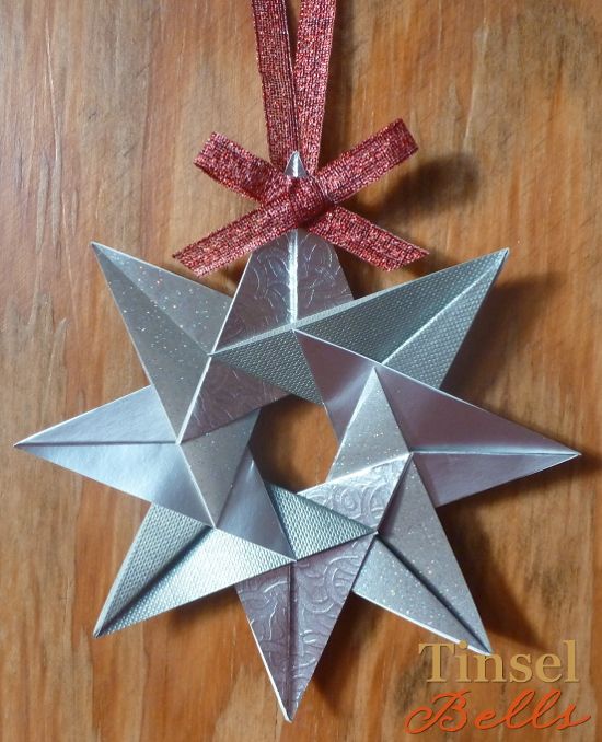 an origami star hanging on a wooden table with a red ribbon around it