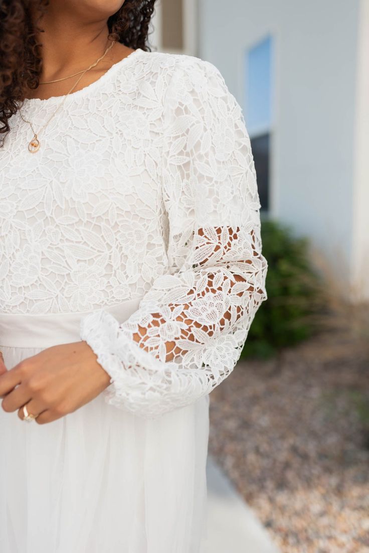 a woman in a white dress is smiling and holding her hand on her hip while standing outside