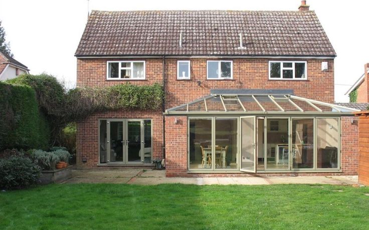 a brick house with an enclosed patio and glass doors on the front, surrounded by lush green grass