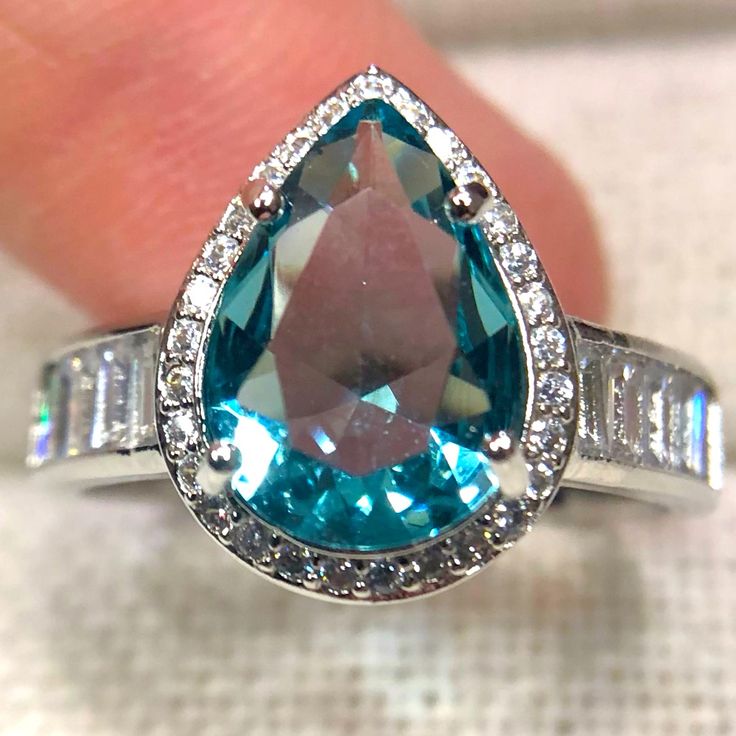 a blue and white diamond ring sitting on top of a table next to a person's hand