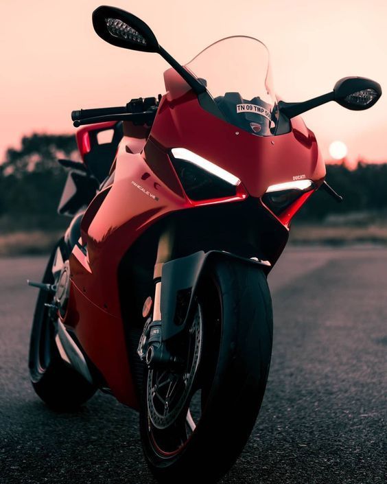 a red motorcycle parked on the side of the road at sunset or dawn with it's lights on