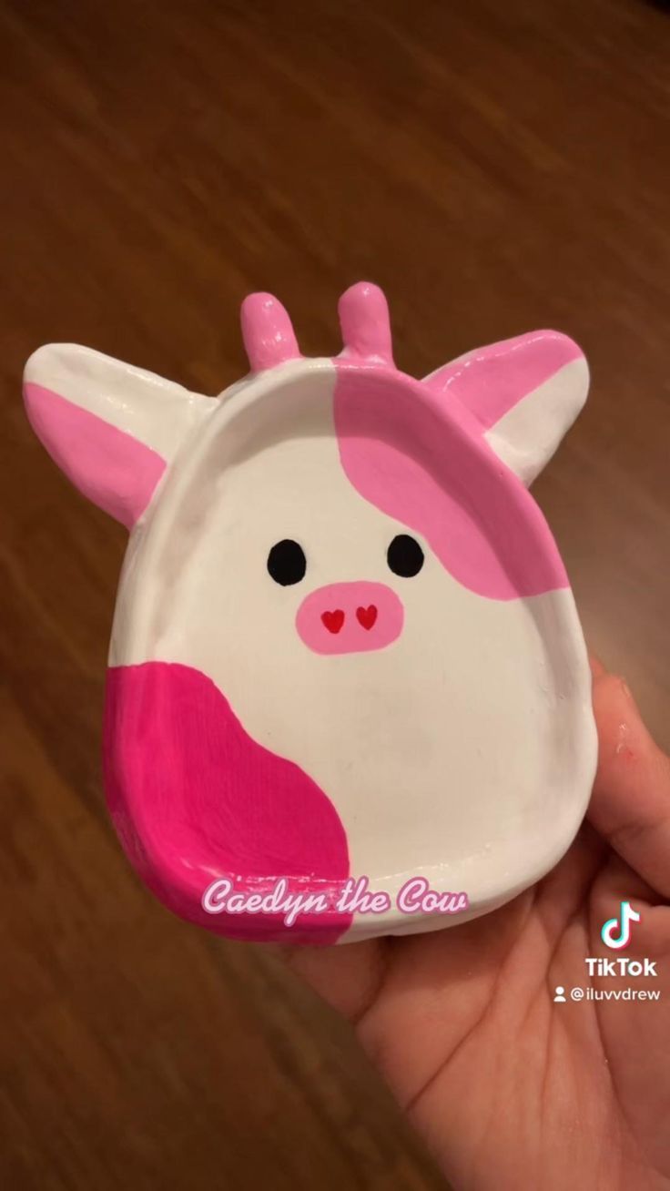 a hand holding a small pink and white cow plate