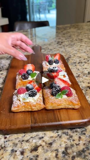 someone cutting up some fruit pizza on a wooden board