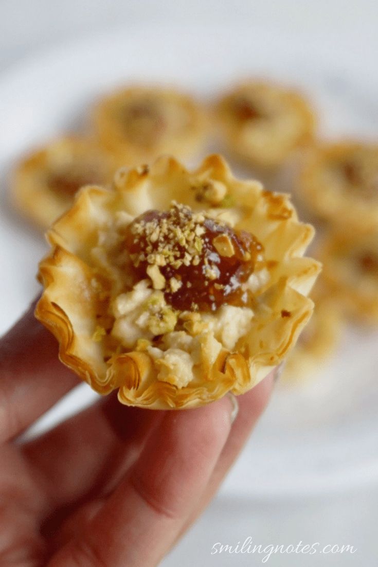 a hand holding a small pastry with toppings on it's top and another plate in the background