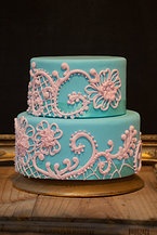 a three tiered cake with blue frosting and pink lace on top, sitting on a wooden table