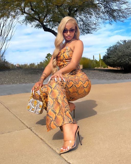 a woman sitting on top of a cement floor next to a tree and holding a purse