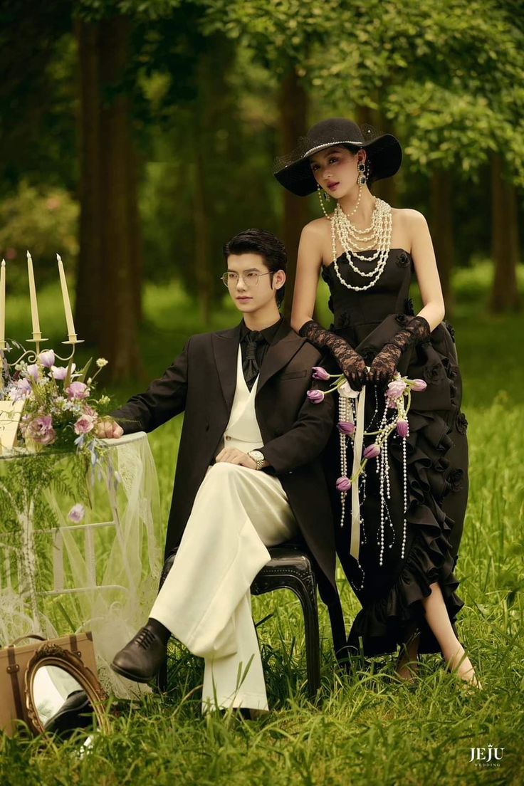 a man sitting next to a woman in a dress and hat on a chair outside