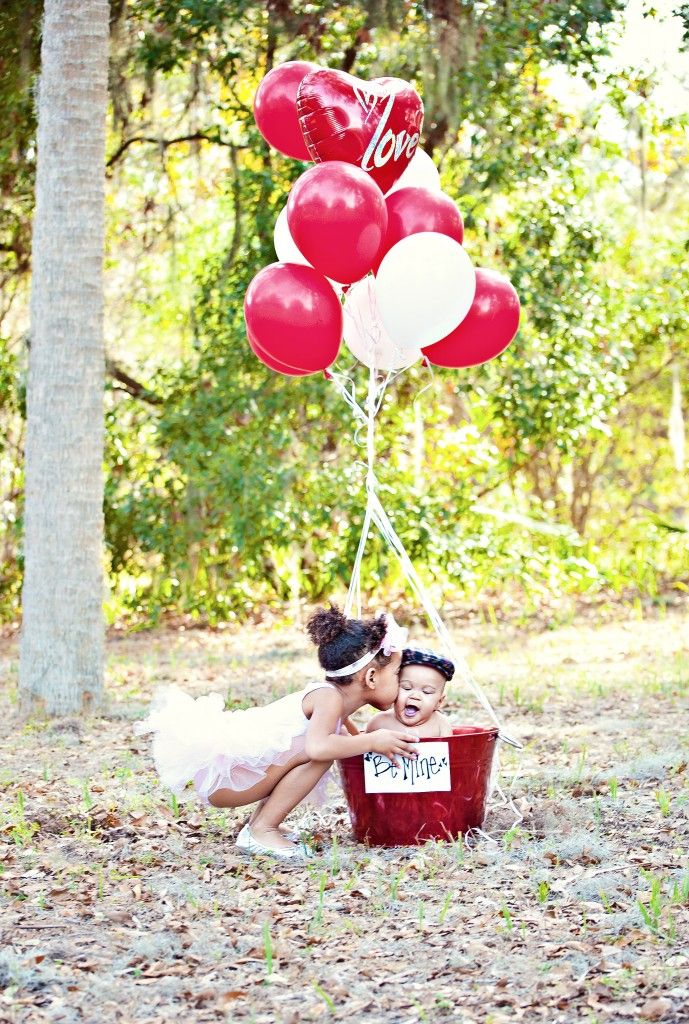 two children are sitting on the ground with red and white balloons