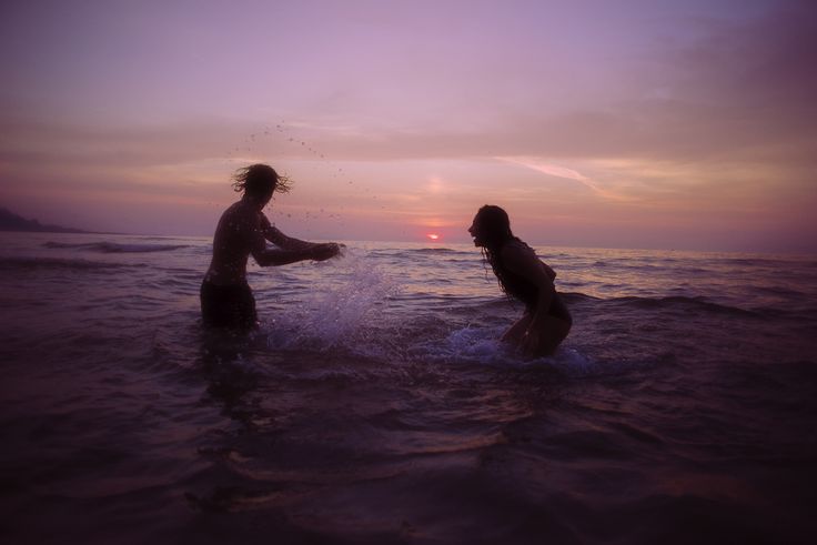 two people playing in the ocean at sunset