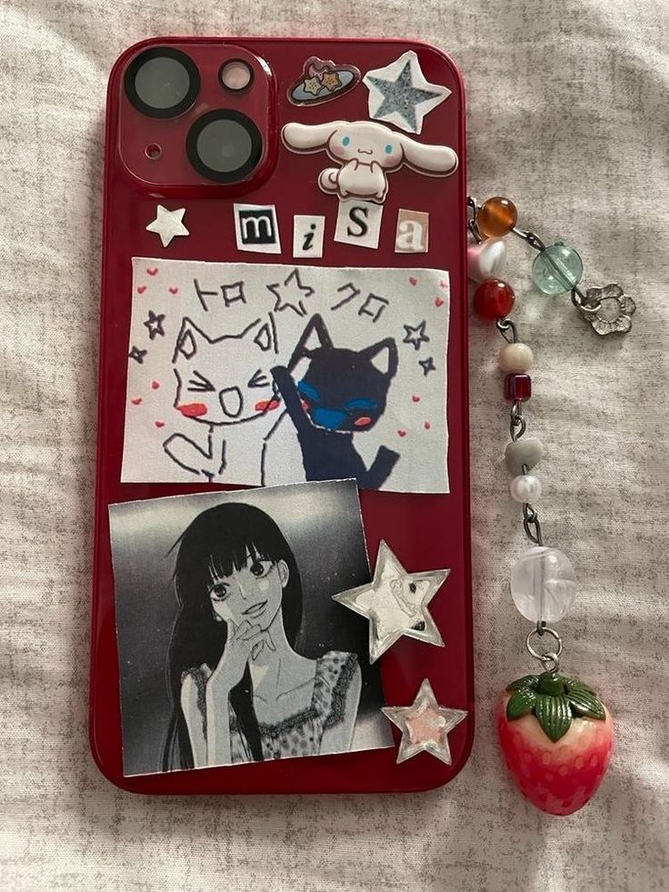 a cell phone with pictures and charms attached to it on a white cloth covered surface