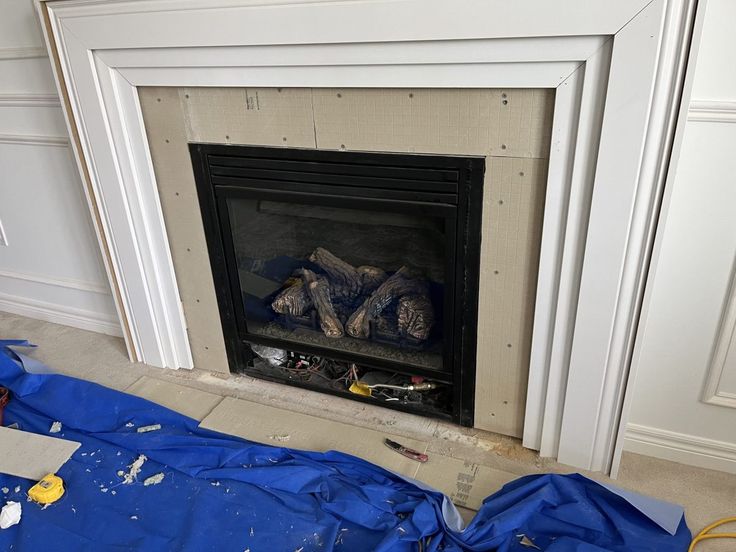 a fire place that is being worked on with blue tarp covering the floor and walls