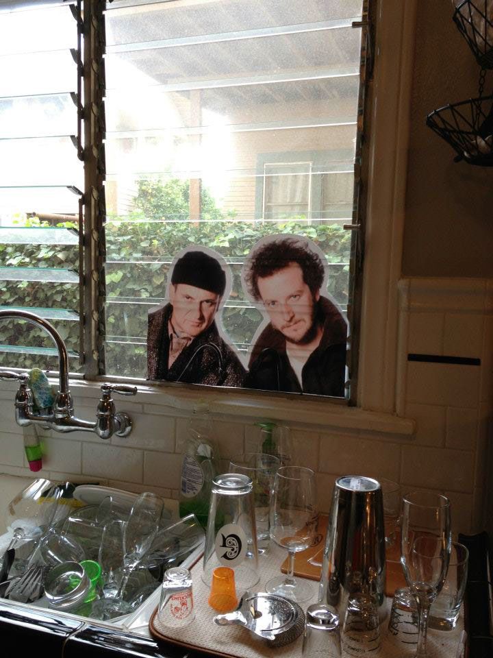 two men are seen in the mirror above a kitchen sink with dishes and glasses on it