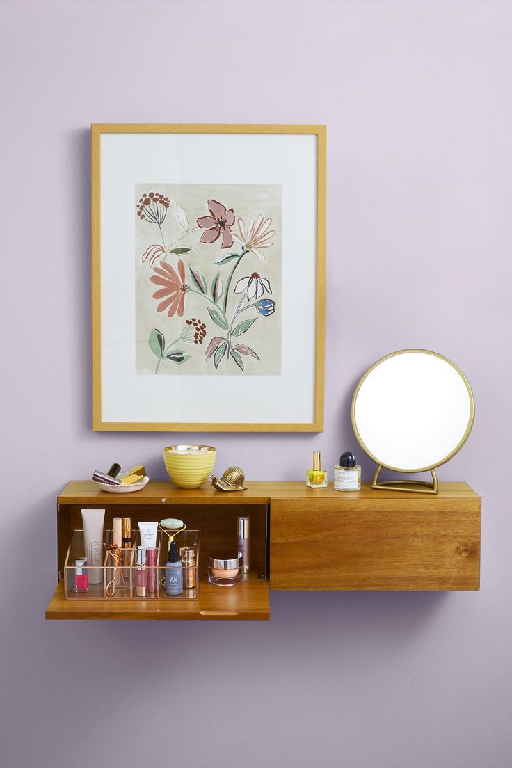 a shelf with various items on it in front of a mirror and framed art piece