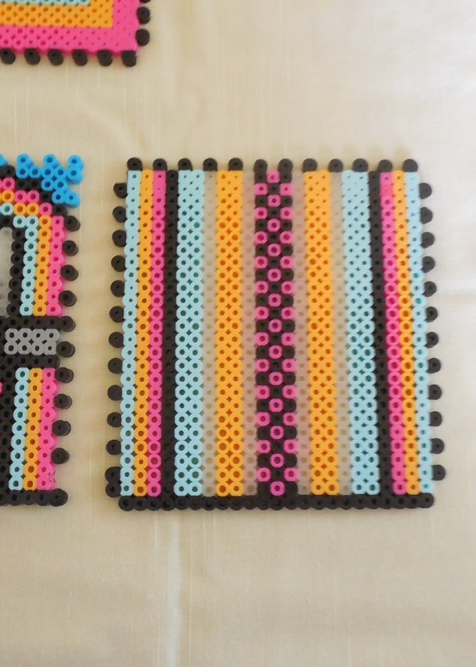 three pieces of perler bead art on a white tablecloth with pink, blue, yellow and orange designs