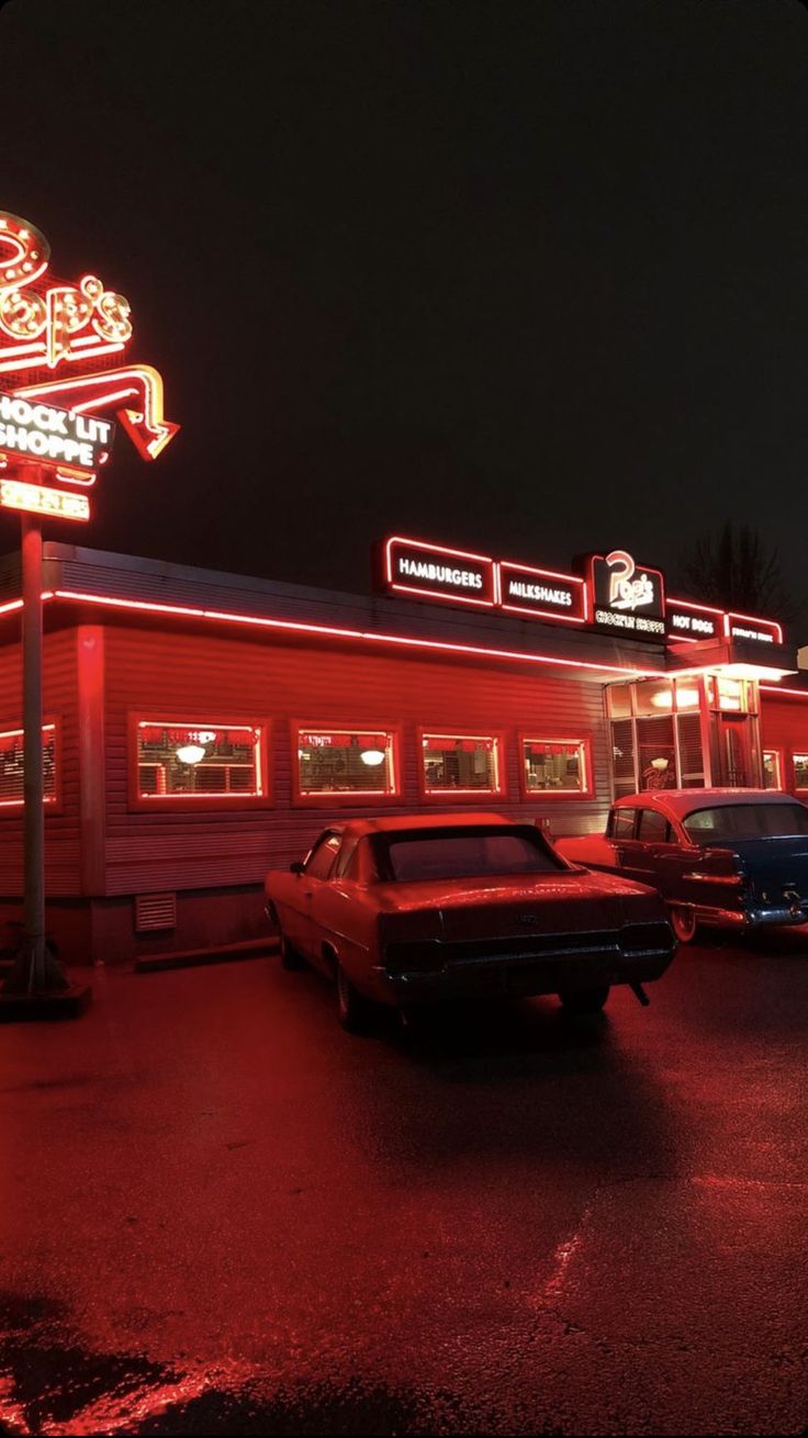 an old car is parked in front of a gas station with neon lights on it