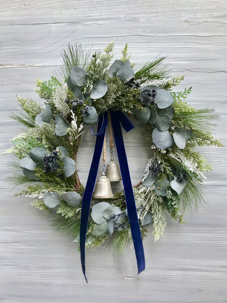 a christmas wreath hanging on the side of a wall with a bell and evergreens