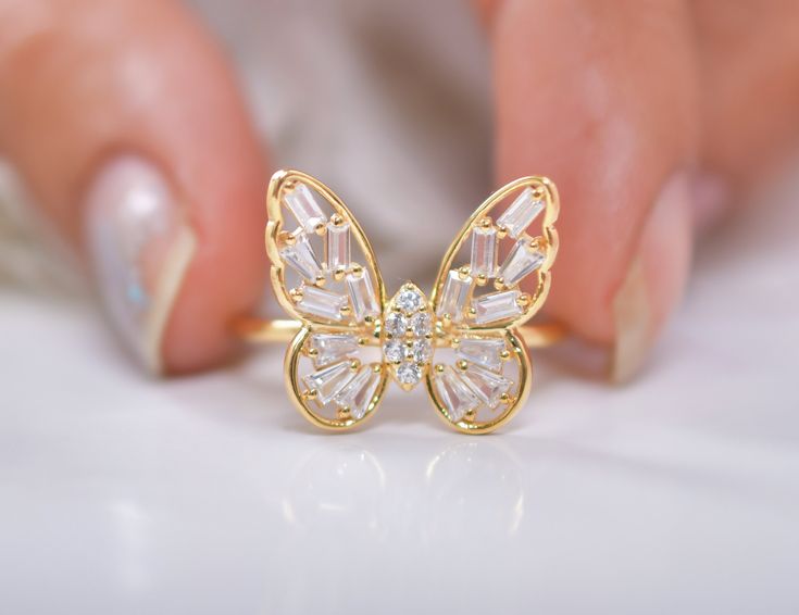 a close up of a person's hand holding a butterfly ring