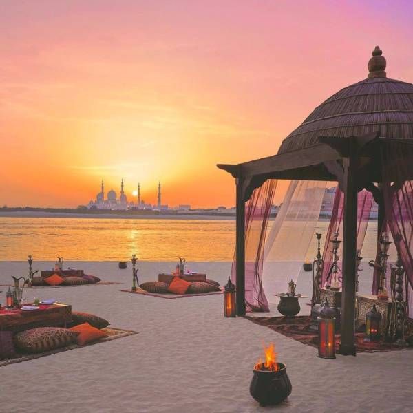 a gazebo sitting on top of a sandy beach next to the ocean at sunset