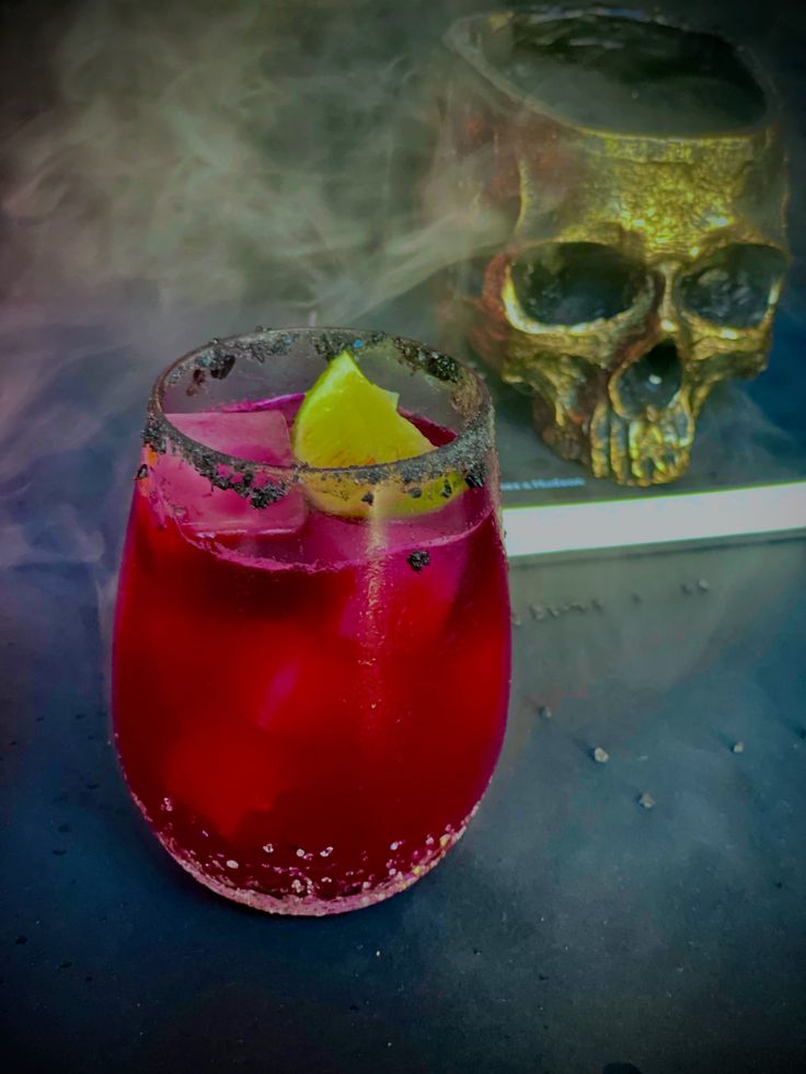 a red drink in a glass with a lemon slice on the rim next to a skull