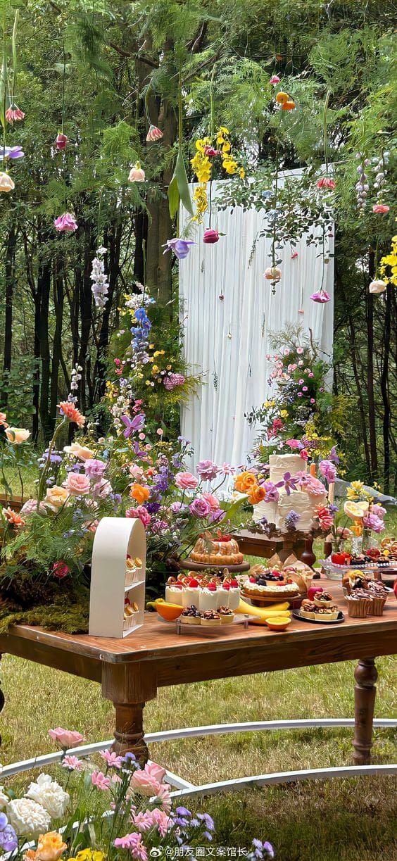 an outdoor table with flowers and cakes on it